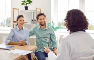 Uśmiechnięta para podczas konsultacji lekarskiej, symbolizująca świadome przygotowanie do ciąży